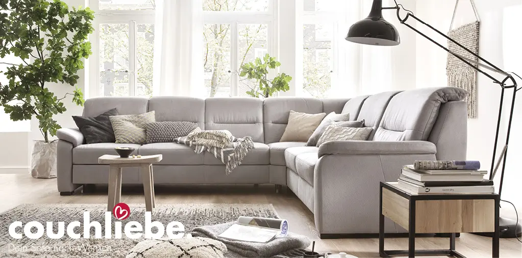 Graues Ecksofa mit Kissen und Decke, runder Holz-Couchtisch auf Teppich, Beistelltisch mit Büchern rechts und Pflanze links im Wohnzimmer, Text couchliebe
